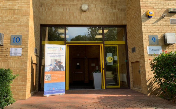 Brick building entrance to MD Support Centre Coventry with yellow-framed glass doors, signage displaying unit numbers 9 and 10, and a banner beside the doorway.